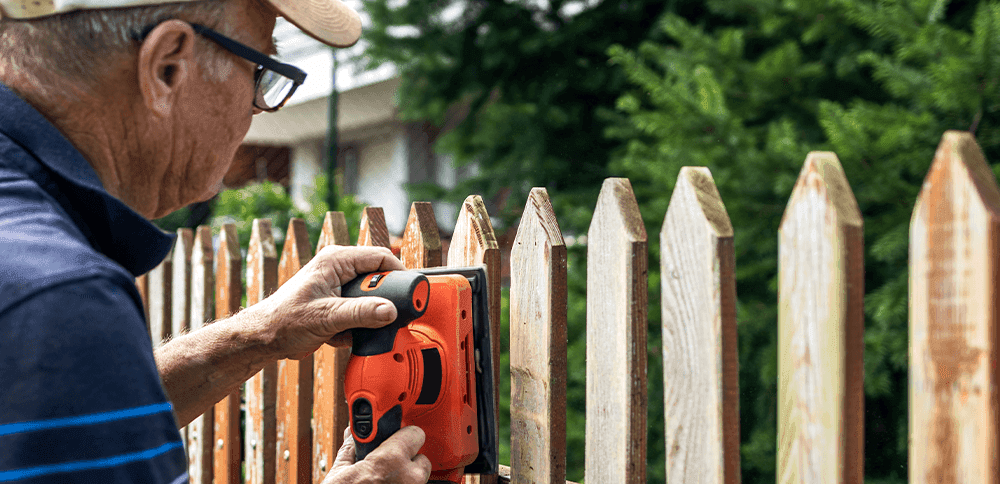 man working on fence with sander